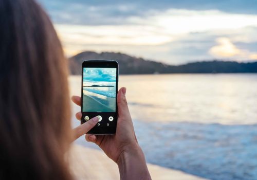 Happy woman taking photos of the sea at sunset with smartphone camera on summer travel vacation to the coast., Phuket island, ThailandBrunette girl making photographie towards the ocean.